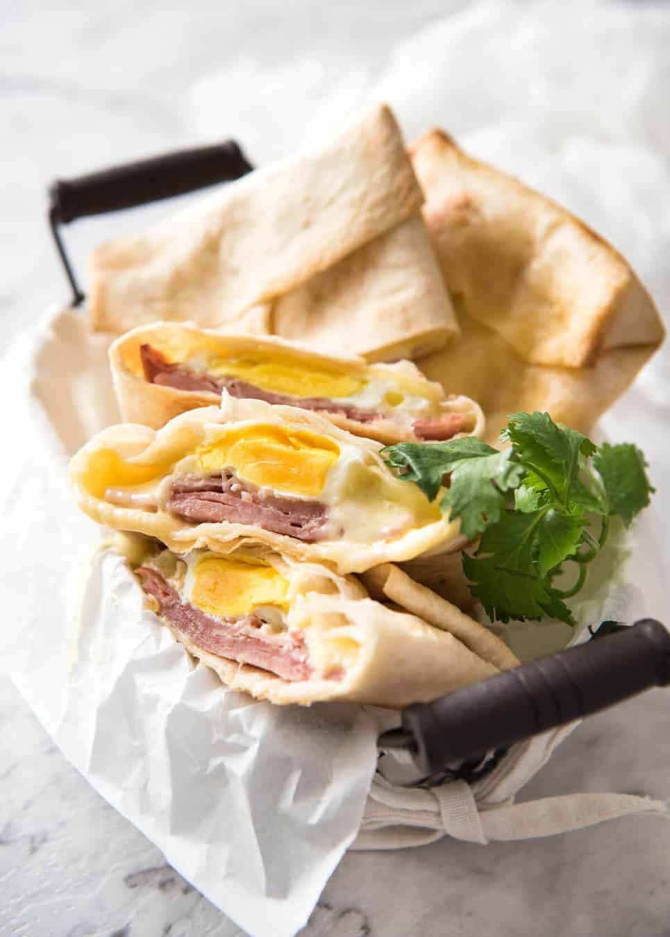 Hot Ham, Egg and Cheese Pockets made with tortillas in a basket, with some cut showing the inside with molten cheese and perfectly cooked egg.